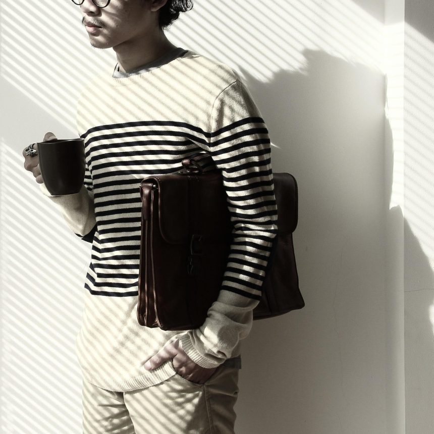 Homem usando óculos de aparência futurista enquanto segura uma xícara de café, em ambiente minimalista com luz e sombra.