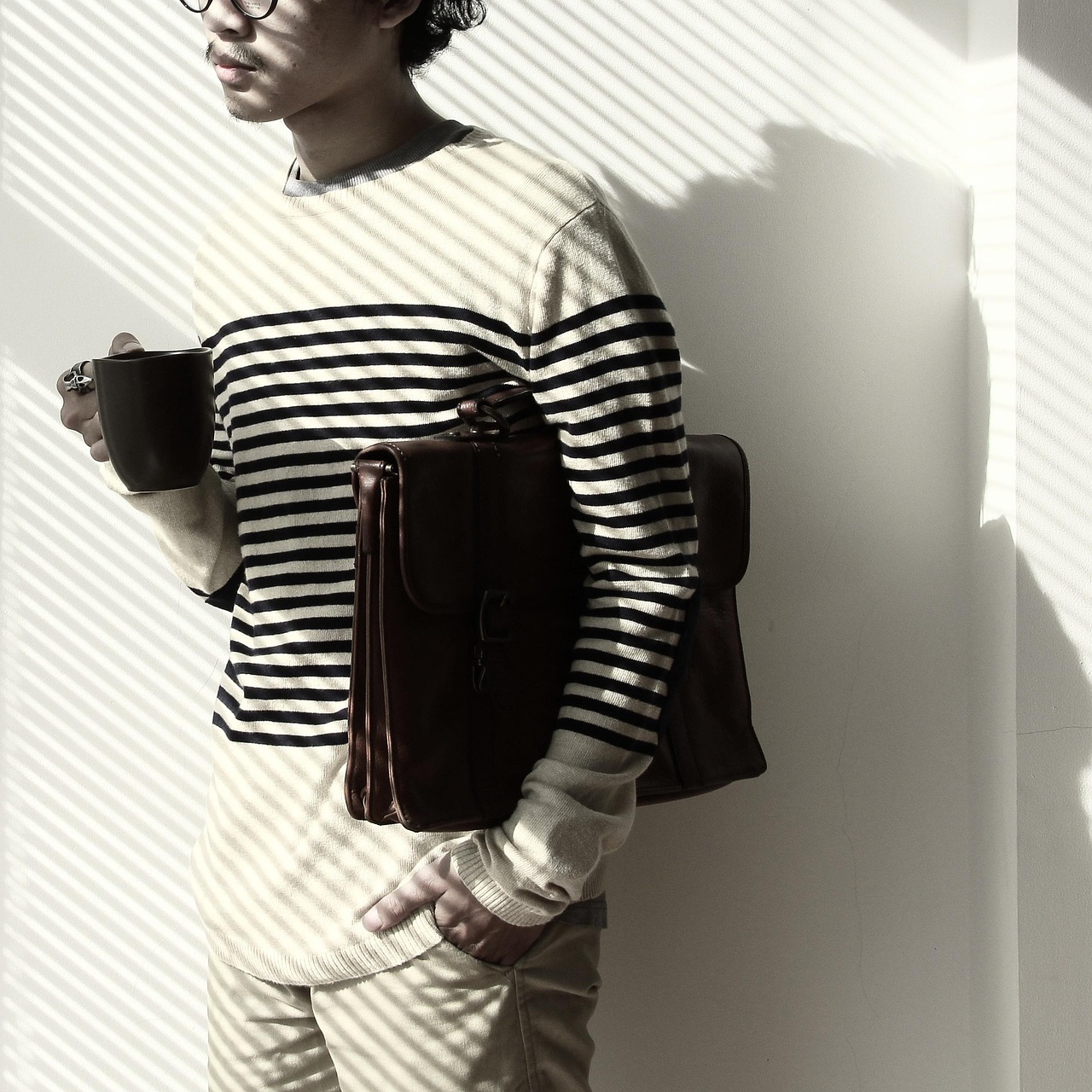 Homem usando óculos de aparência futurista enquanto segura uma xícara de café, em ambiente minimalista com luz e sombra.